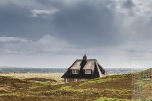 Reetdachhaus steht in den Dünen von Hörnum im Süden der Insel Sylt. Am Horizont ist die Küstenlinie der Nachbarinsel AMrum zu sehen